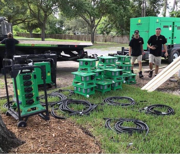 Lawn with SERVPRO equipment set on the ground and two male employees conversing